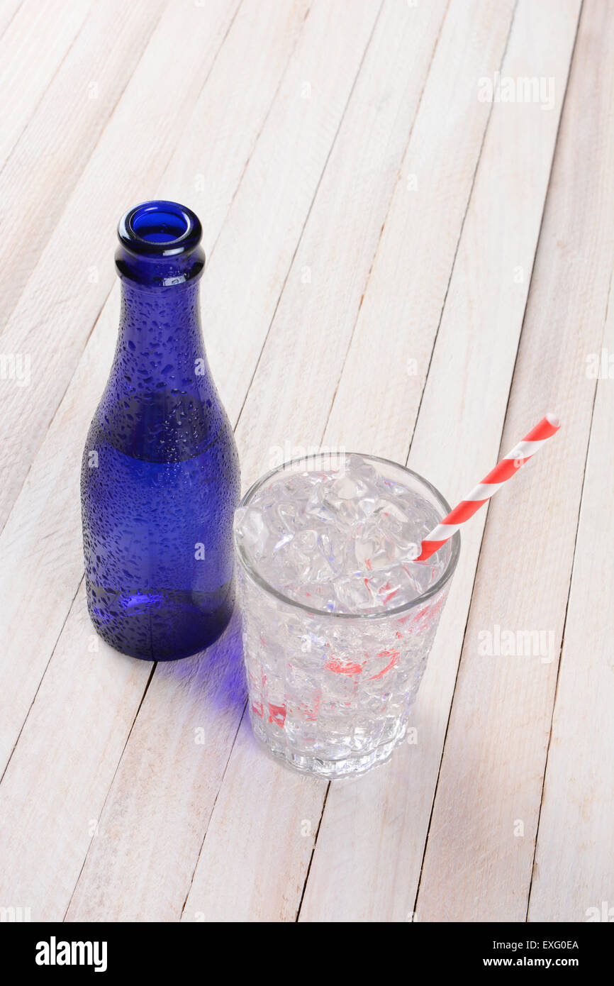 Hohen Winkel Schuss ein Glas voller Wasser und Eis und rot und weiß Stroh neben einer blauen Flasche zu trinken. Hochformat mit co Stockfoto