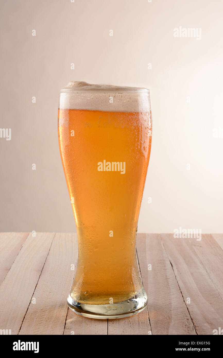Ein Glas Bier auf einem rustikalen Holztisch mit einer leichten bis dunkelgrauen Hintergrund. Stockfoto