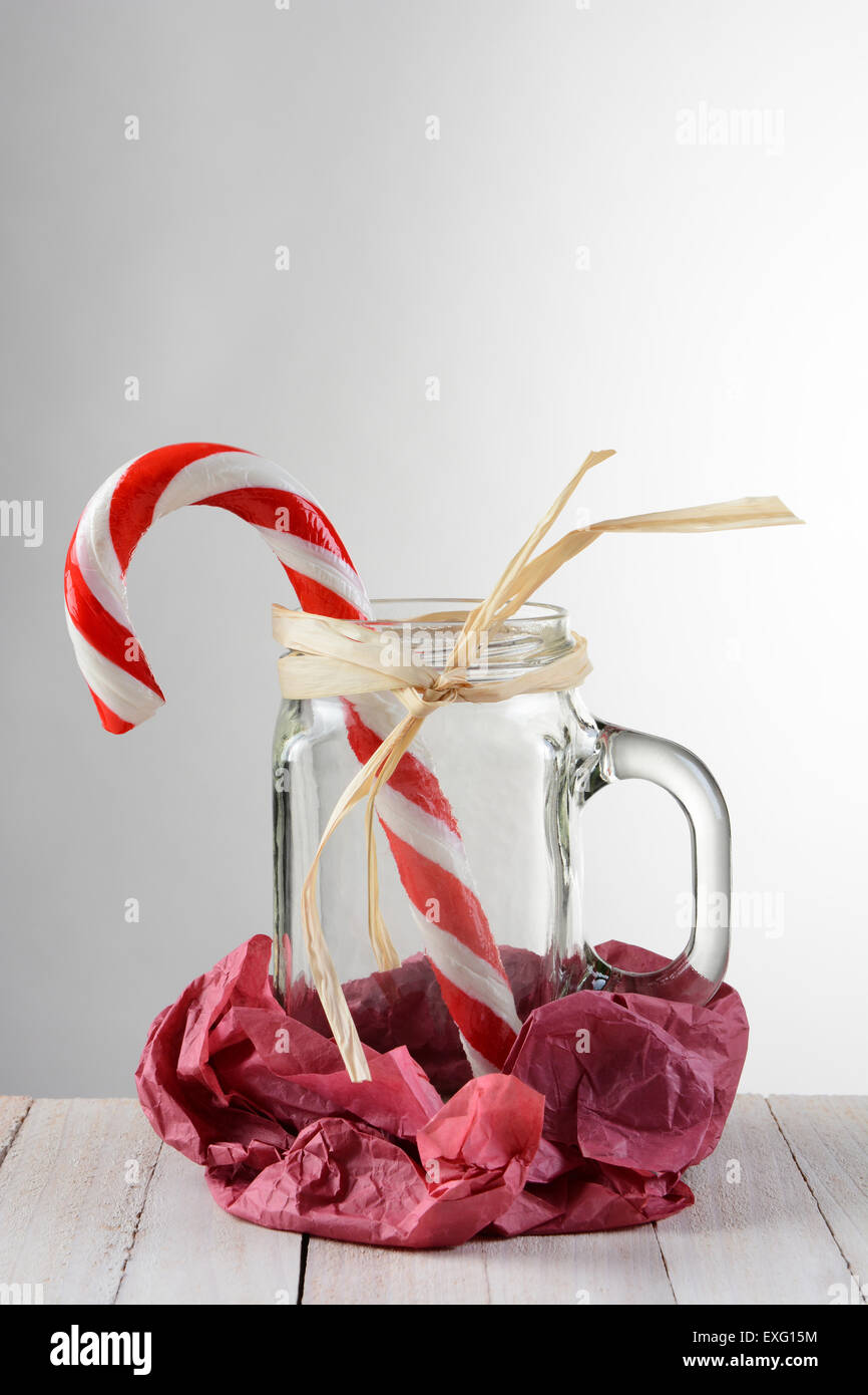 Eine große Zuckerstange in einem Mason Stil Glas mit Griff gegen eine leichte bis dunkelgrauen Hintergrund. Das Glas wird in zerknitterten roten Ti festgelegt. Stockfoto