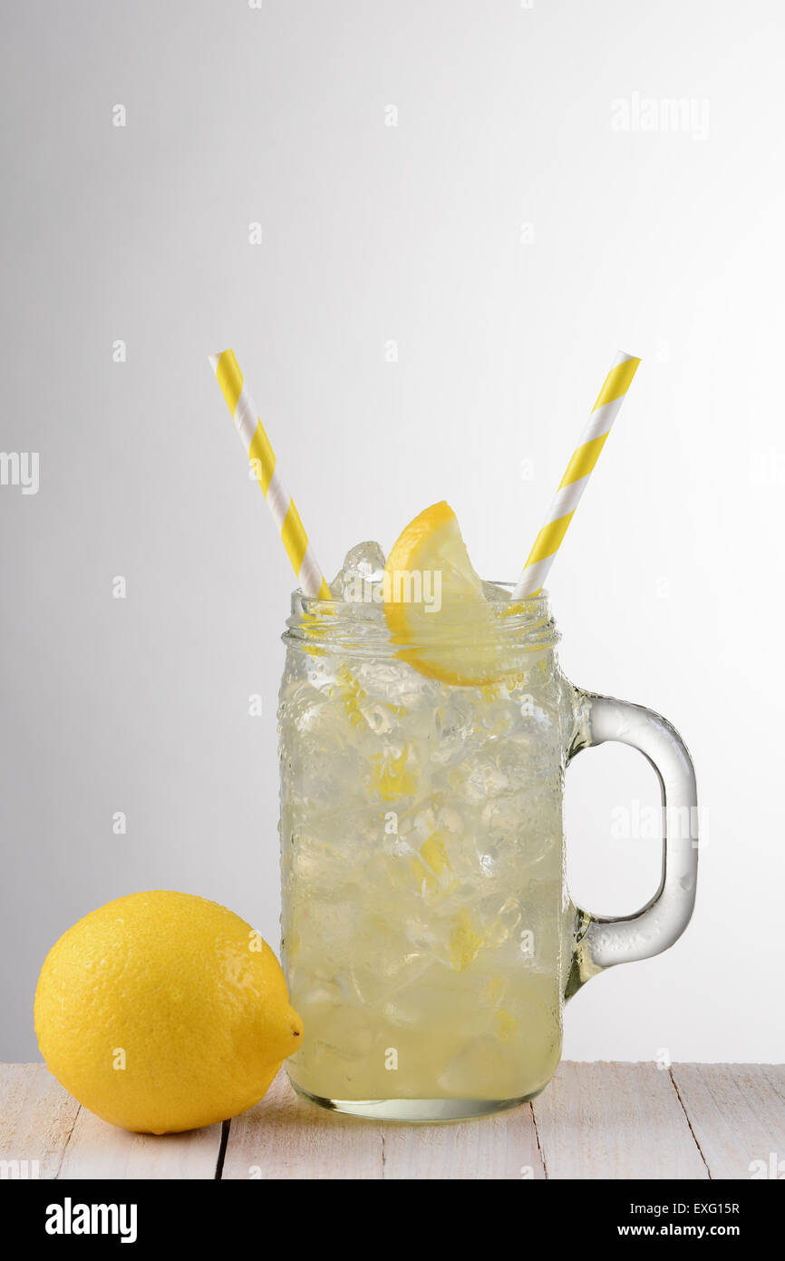 Nahaufnahme eines Glases Limonade mit zwei gelben Strohhalme. Auf einem rustikalen Holztisch mit ganzen Zitronen und ein Licht auf dunklen grauen staatlich Stockfoto
