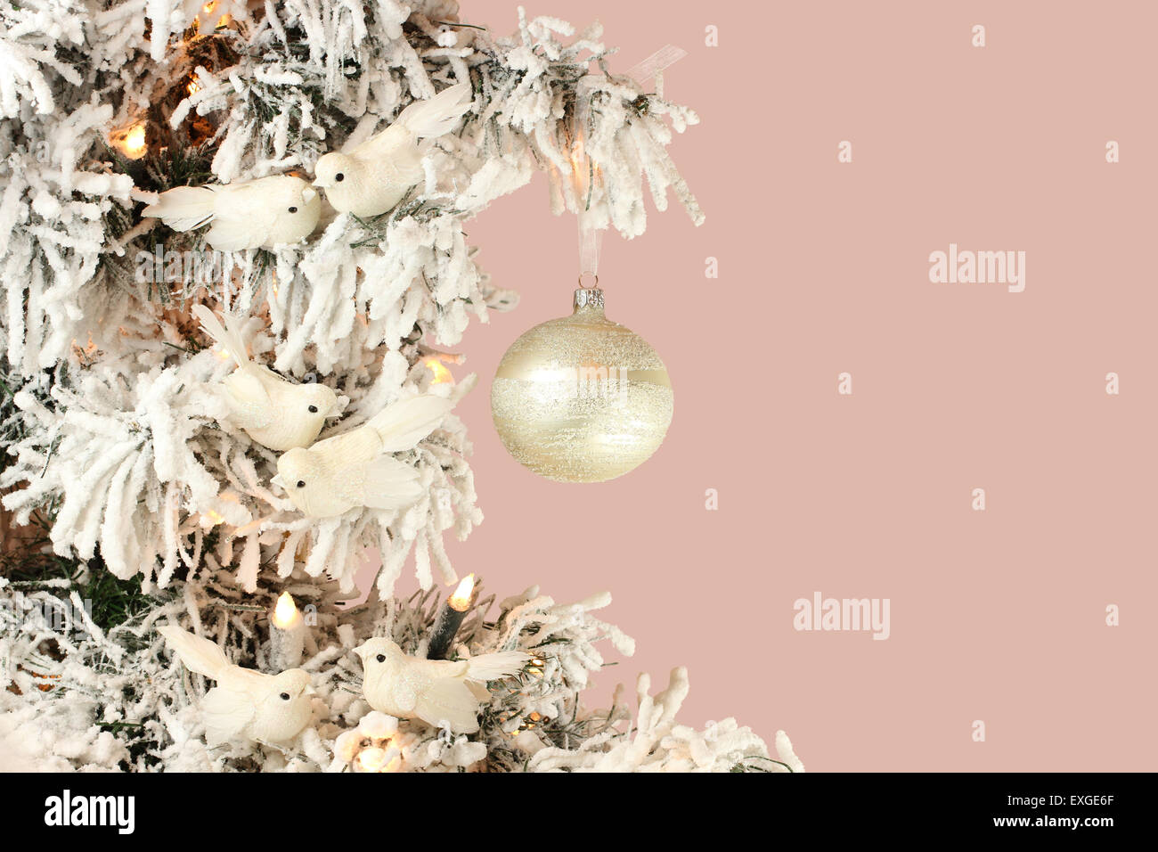 Dekoration am Weihnachtsbaum - weiße Vögel und Silberkugel auf schneebedeckten Fichten auf rosa Hintergrund Stockfoto