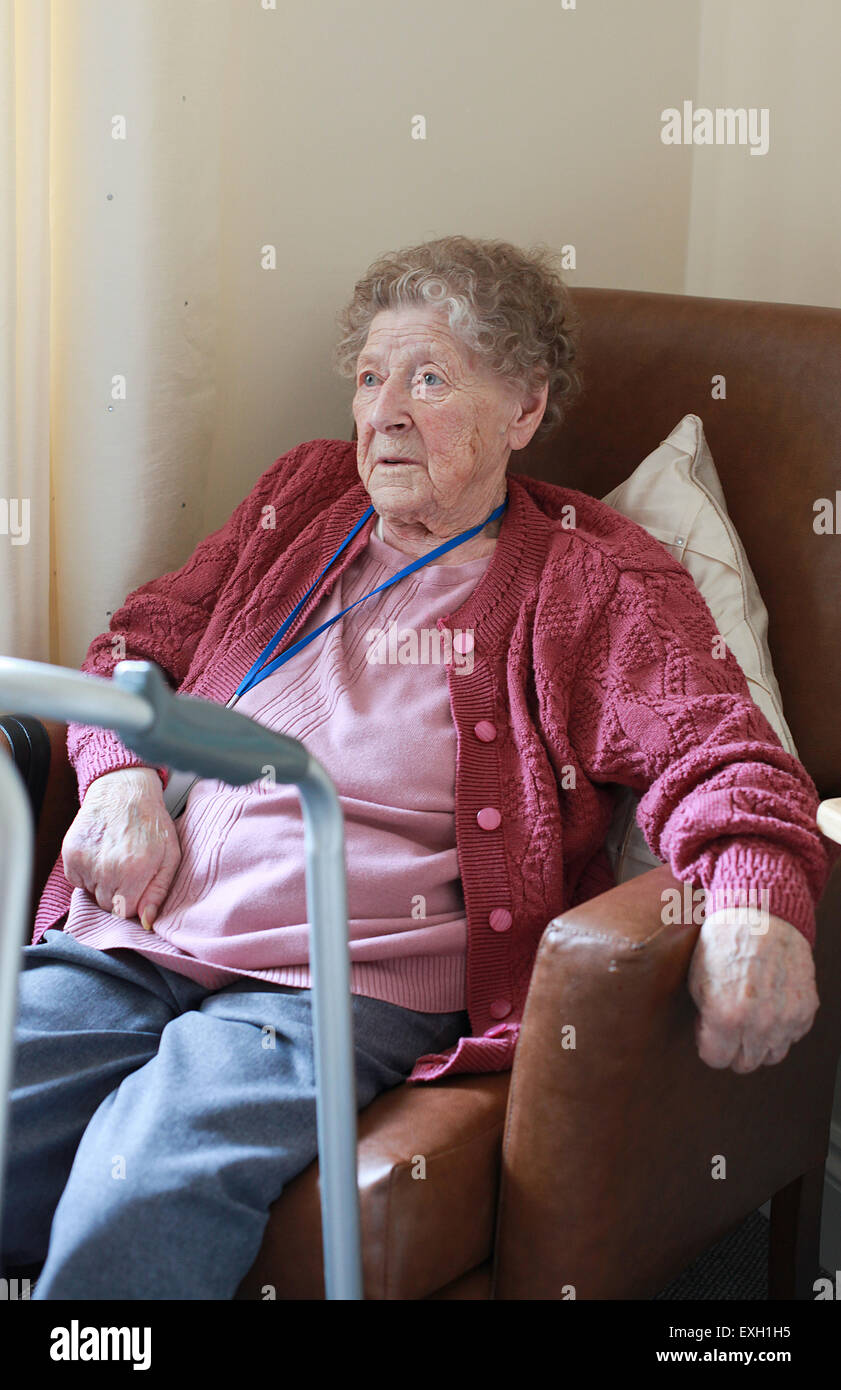 Bildnis einer älteren Dame sitzt in einem Sessel in ein Pflegeheim mit ihren remote-Unterstützung um den Hals. Stockfoto