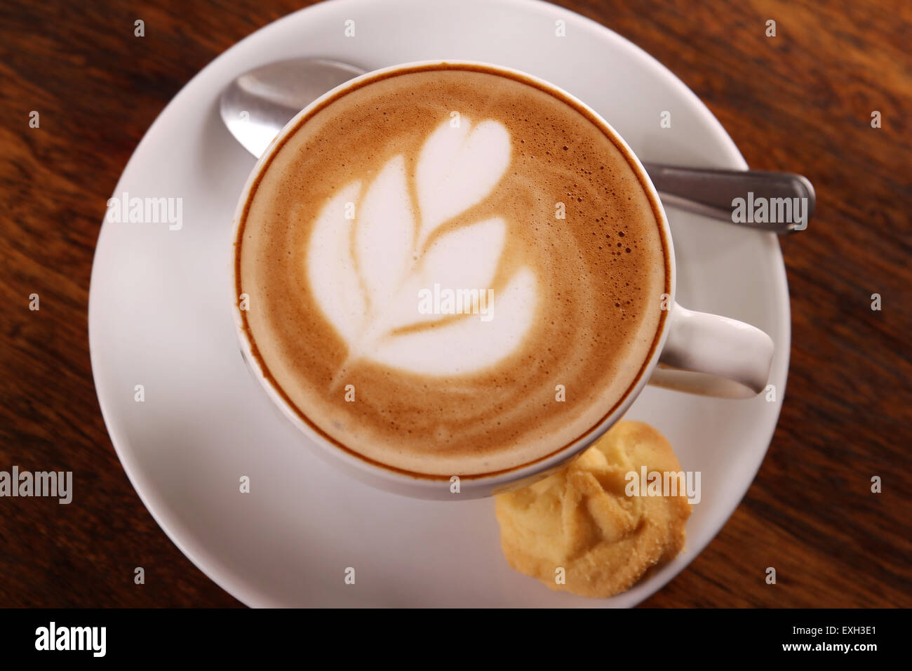 Köstlich aromatischen Cappuccino in einer weißen Porzellantasse mit einem Keks auf der Seite auf einem Holztisch. Stockfoto