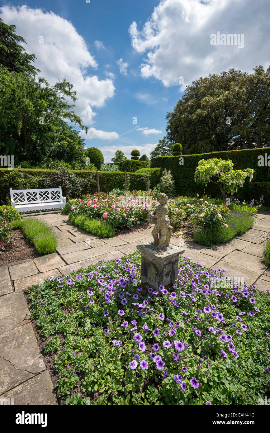 Die Flagge Garten Arley Hall in Cheshire. Eine Statue und Sitzbank umgeben von Rosen und Sommer Bettwäsche. Stockfoto