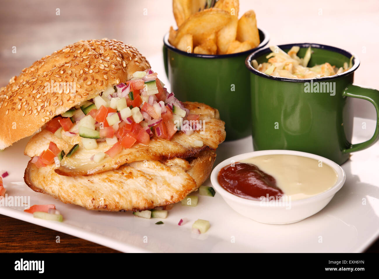 Leckere Hähnchen-Burger mit gehackten Salat serviert mit Kartoffelecken auf einem weißen Teller auf einem Holztisch. Stockfoto