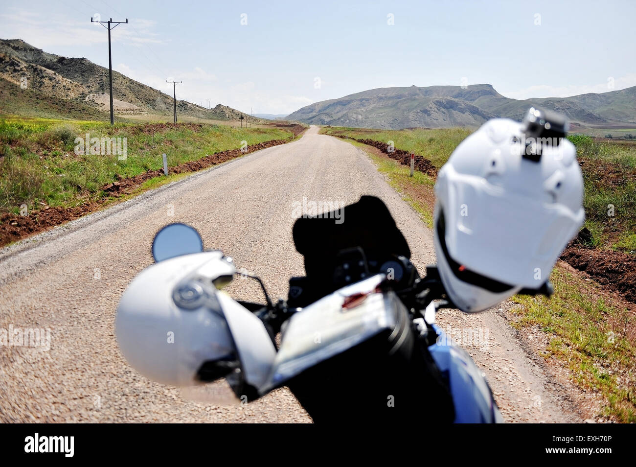 Zwei weiße Helme auf einem Motorrad-Lenker auf einer leeren Landstraße Stockfoto