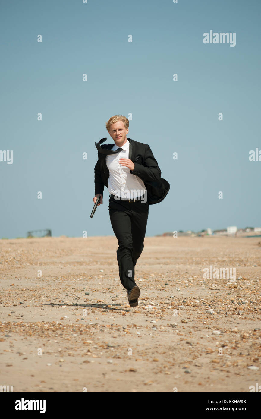 Mann hält eine Pistole und eine lange laufen am Strand in einem schwarzen  Anzug Stockfotografie - Alamy