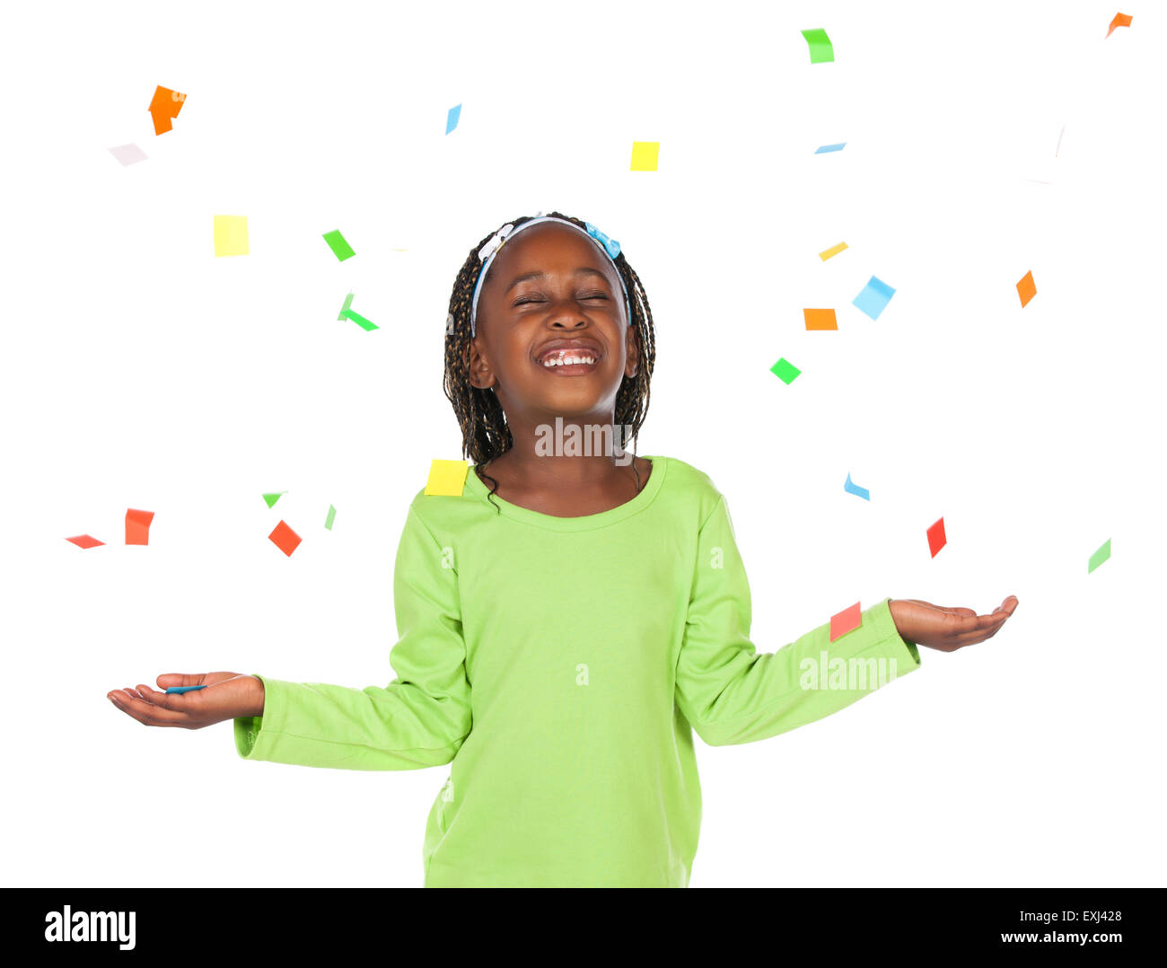 Entzückenden kleinen afrikanischen Kind mit Zöpfen trägt ein leuchtendes grünes Hemd. Sie hält ihre Hände unter fallenden Konfetti. Stockfoto