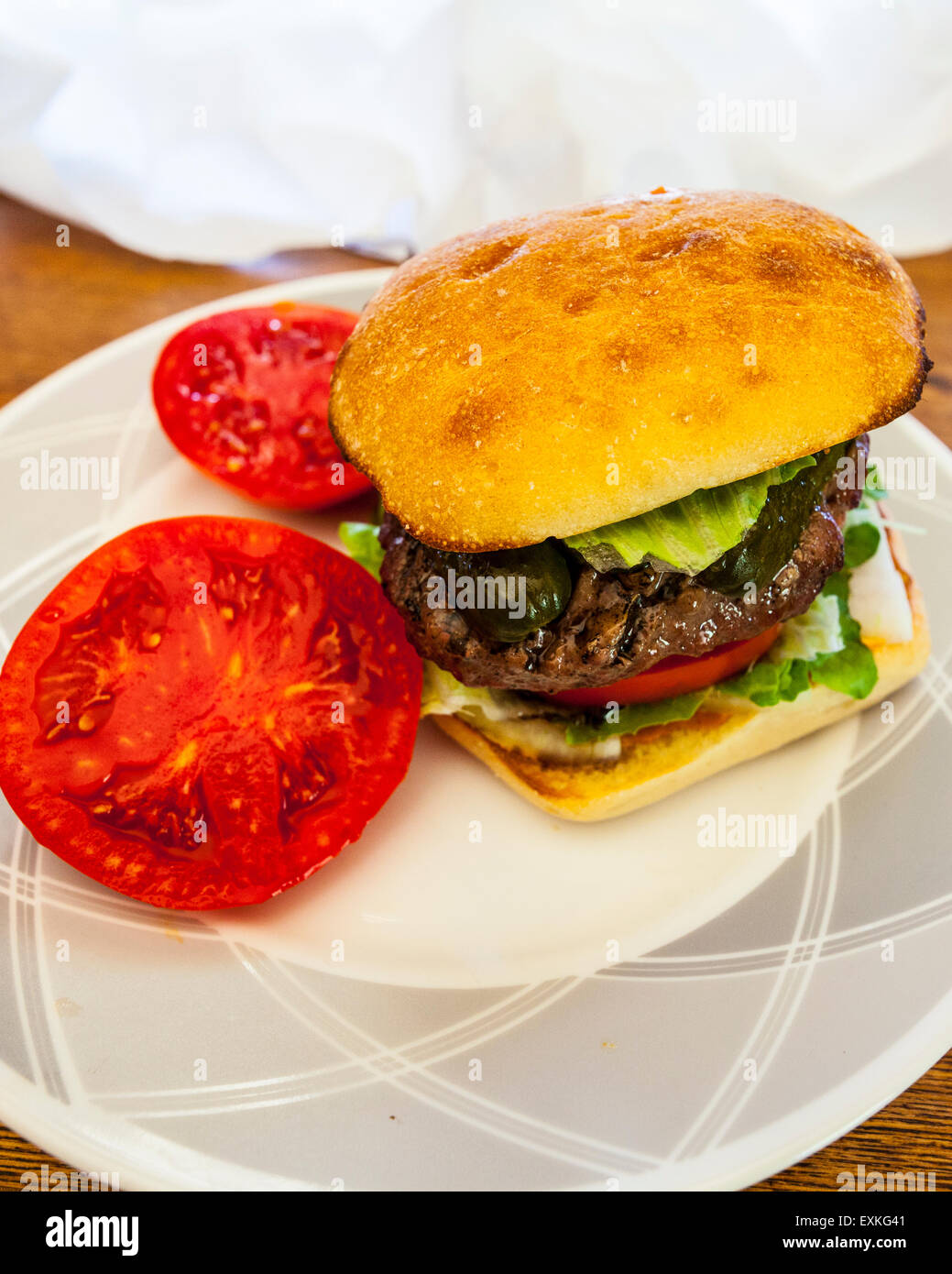 Ein Hamburger auf einem Torta Rollen mit frischen hausgemachten Tomaten aus dem Garten mit Gurke und Römersalat auf einem Tisch für das Mittagessen Stockfoto