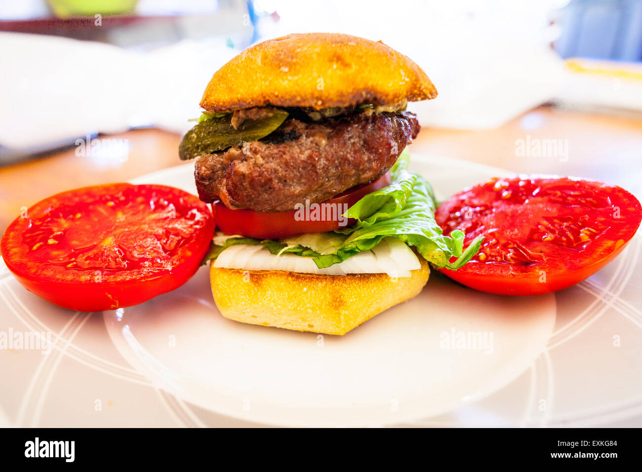 Ein Hamburger auf einem Torta Rollen mit frischen hausgemachten Tomaten aus dem Garten mit Gurke und Römersalat auf einem Tisch für das Mittagessen Stockfoto