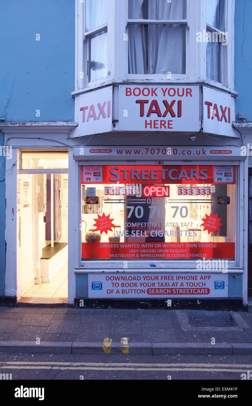 Buchen Sie Ihr Taxi hier. Die hellen Abend licht und Werbung Zeichen der Straßenbahnen Taxiunternehmen Büro. Dorchester, Dorset, England, Vereinigtes Königreich. Stockfoto