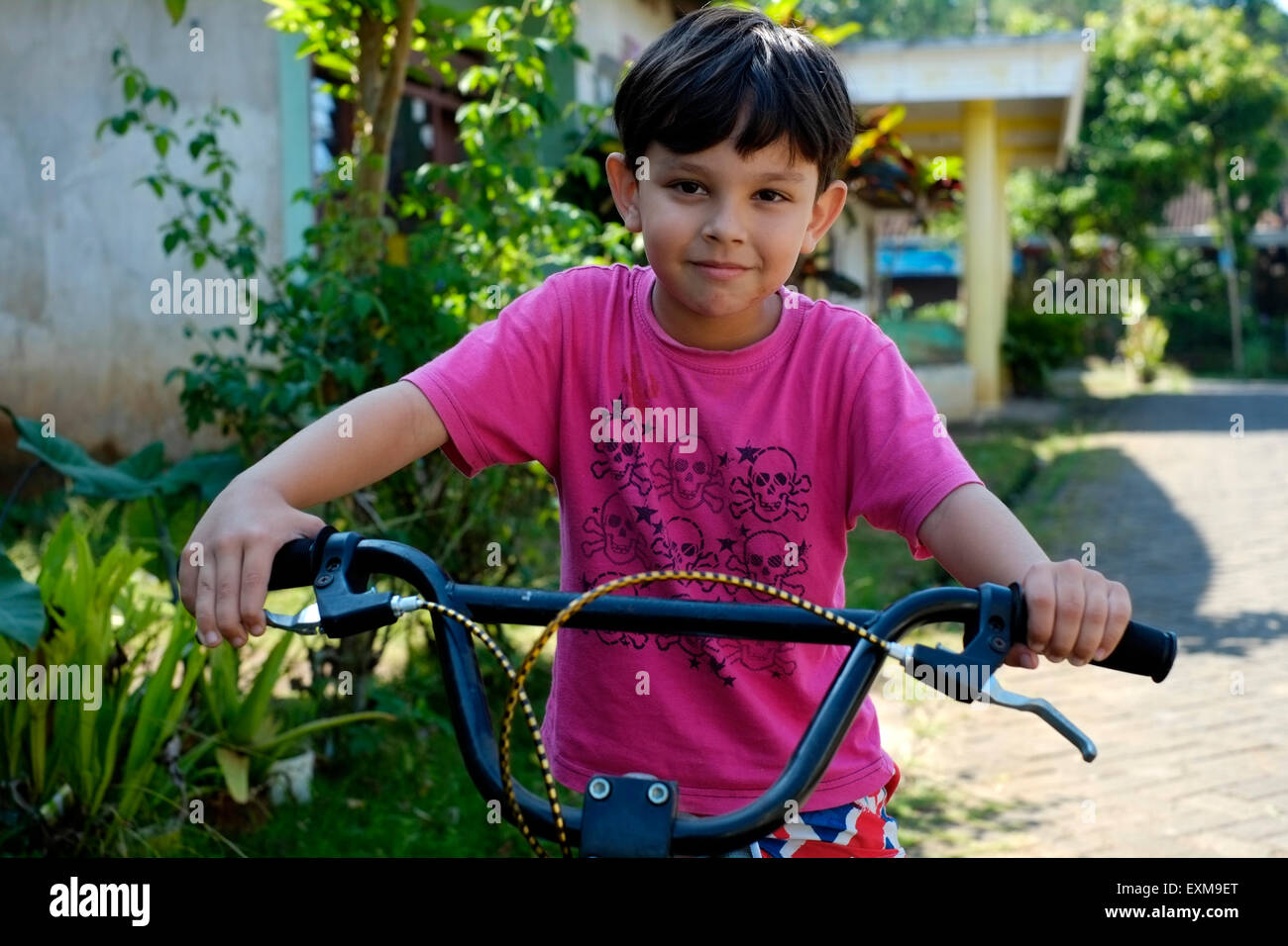 sieben Jahre alten kleinen Jungen auf seinem Fahrrad in einer Dorfstraße in Java Indonesien spielen Stockfoto