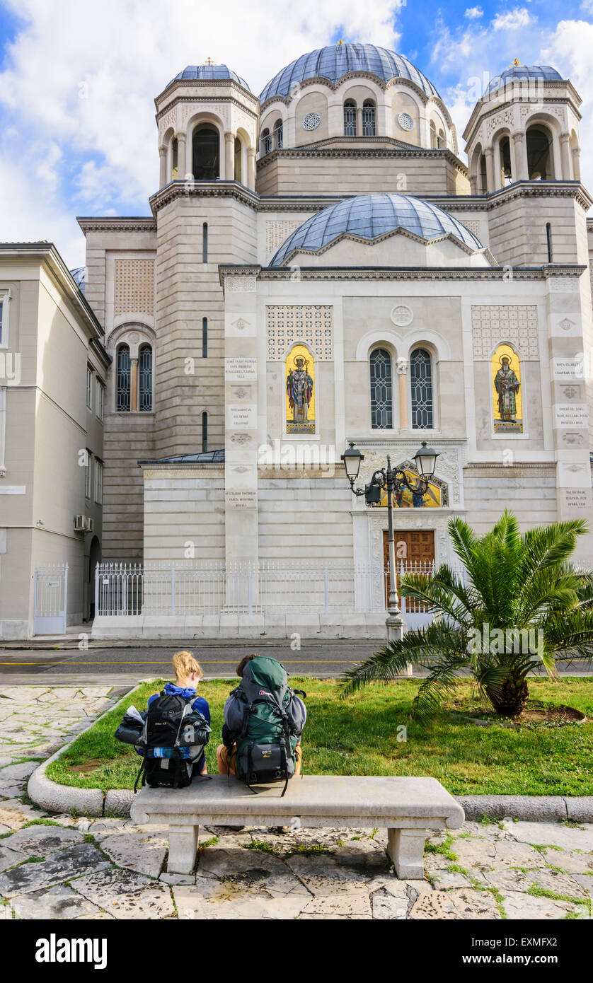 Zwei Backpacker sitzen auf einer Bank außerhalb St. Spyridon Kirche, Triest, Italien Stockfoto