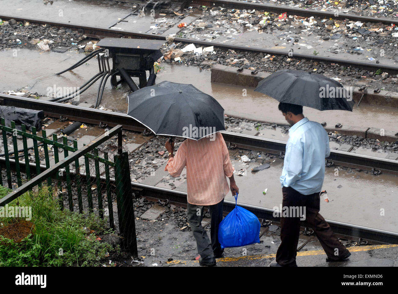 Pendler gehen mit ihren Regenschirmen offen auf die Bahngleise bei Regen am Kurla Statio Mumbai; Maharashtra; Indien Stockfoto