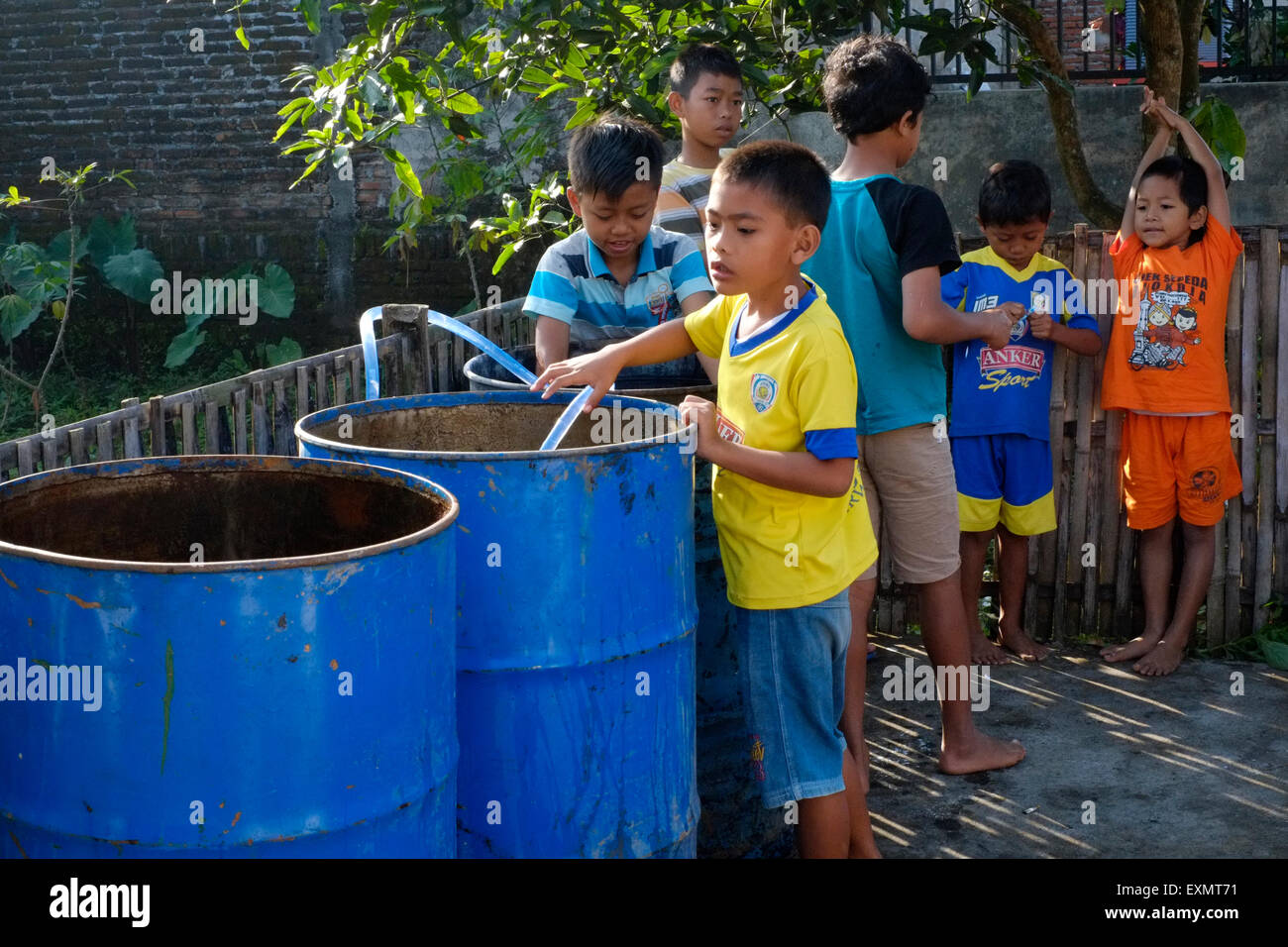 junge Dorfkinder spielen mit Wasser aus großen Öl-Trommeln in einem ländlichen Dorf in Java Indonesien Stockfoto