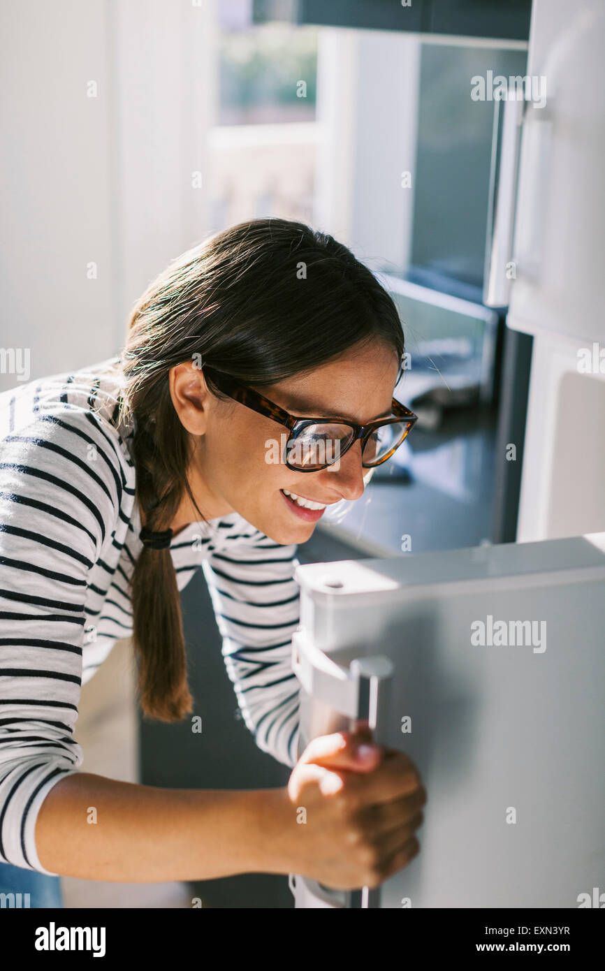 Junge Frau, die Kühlschranktür öffnen Stockfoto