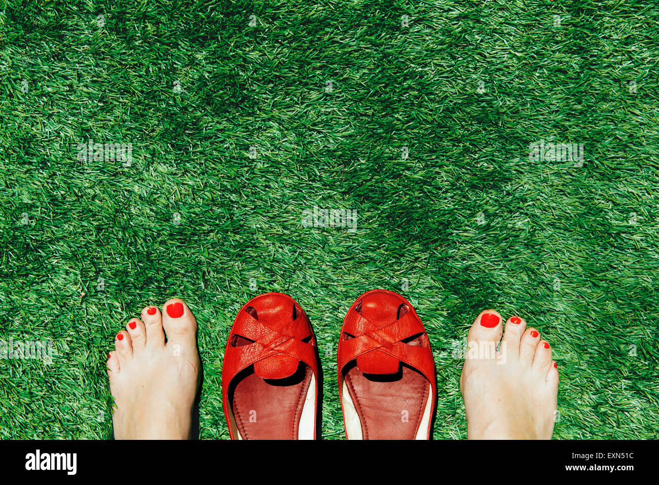 Barfuß Frauen mit Nägeln neben ein paar rote Schuhe auf dem grünen Rasen rot lackiert Stockfoto