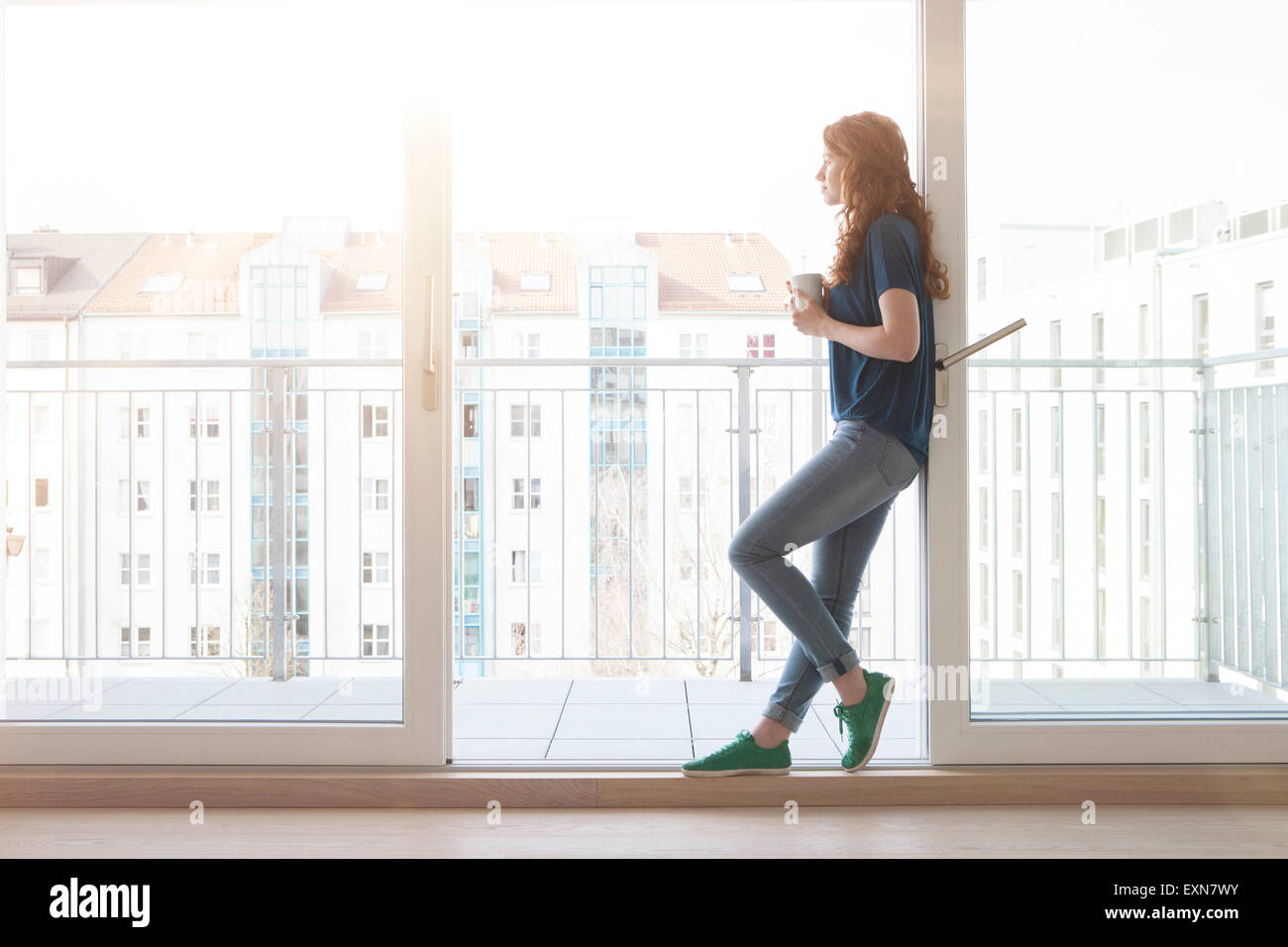 Junge Frau lehnt sich an Schiebetür der Balkon mit Blick auf Distanz Stockfoto