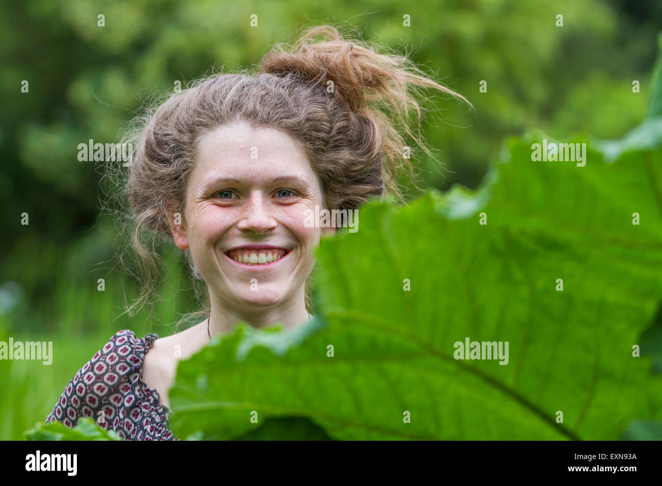 Porträt der lächelnde junge Frau mit Brötchen hinter einem Blatt Stockfoto