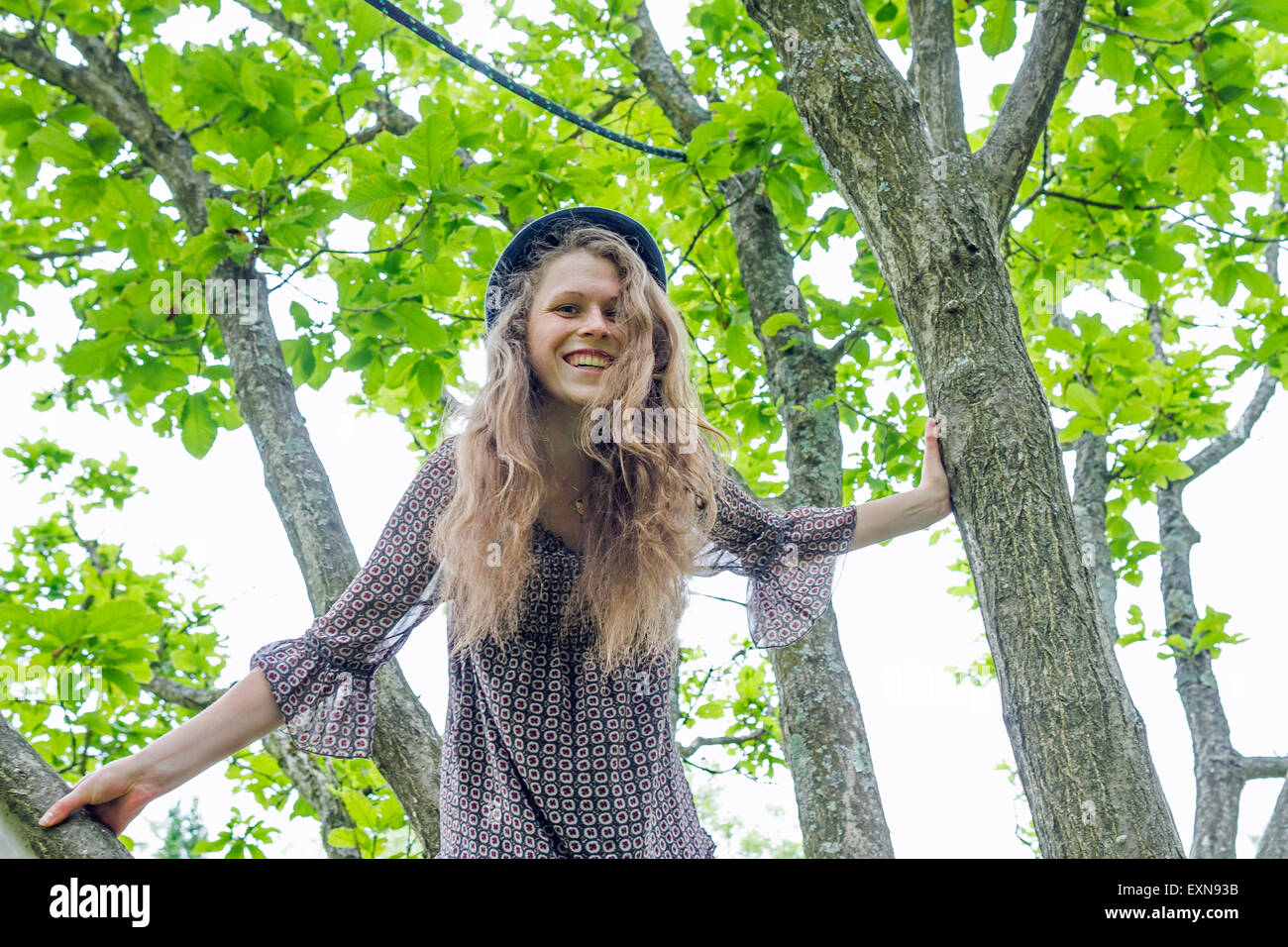 Porträt der lächelnde junge Frau, die auf einen Baum klettern Stockfoto