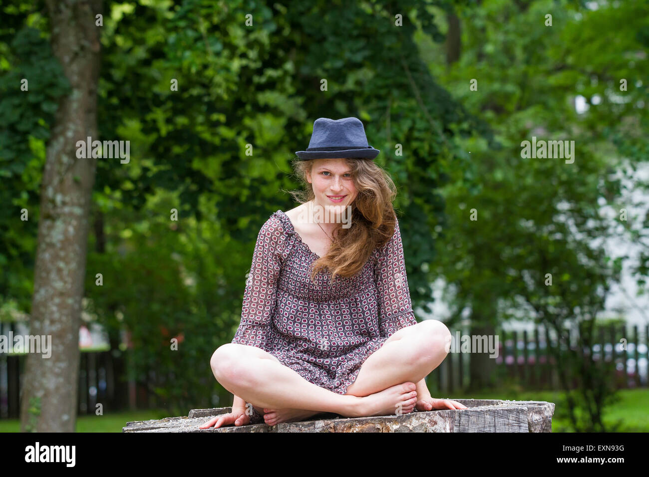 Porträt der lächelnde junge Frau mit Hut auf Baumstamm sitzend Stockfoto