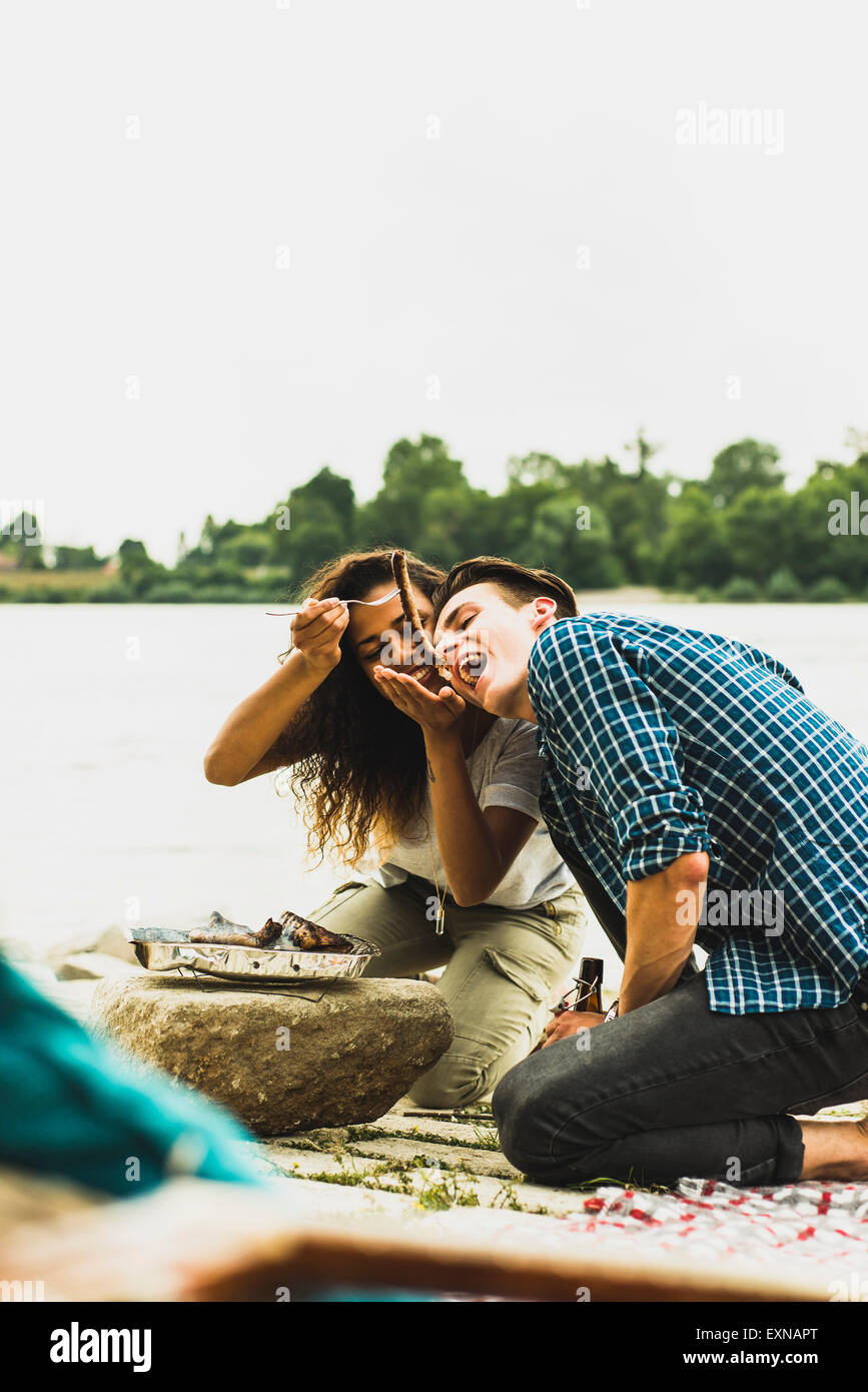 Glückliches junges Paar beim Grillen am Flussufer Stockfoto