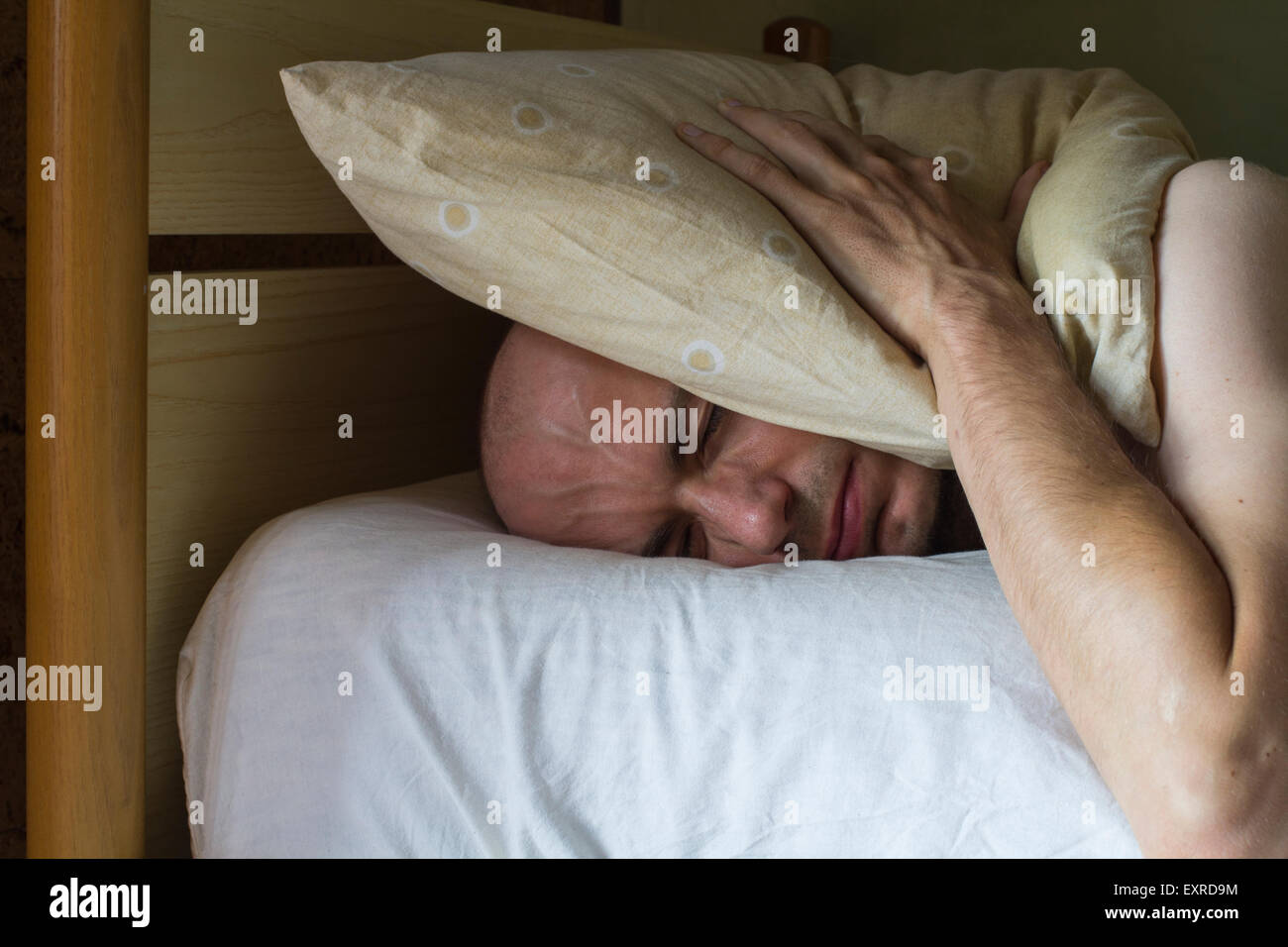 Weißer Mann auf dem Bett mit einem Kissen über dem Kopf am Tag Stockfoto