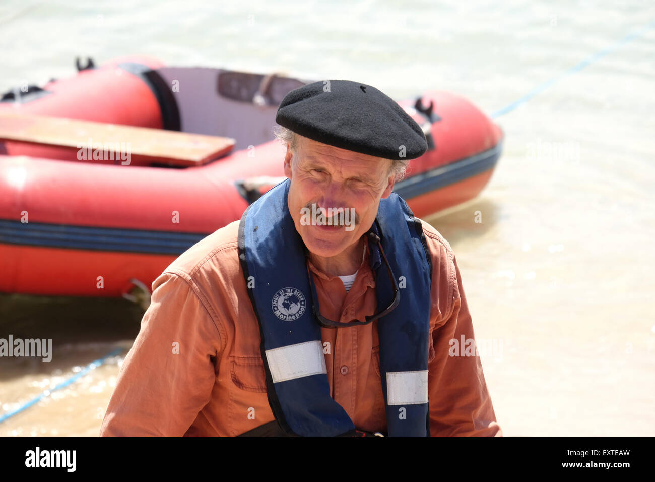 St. Ives, Cornwall, UK: Mann in Barett und Schwimmweste mit Beiboot im Hintergrund. Stockfoto