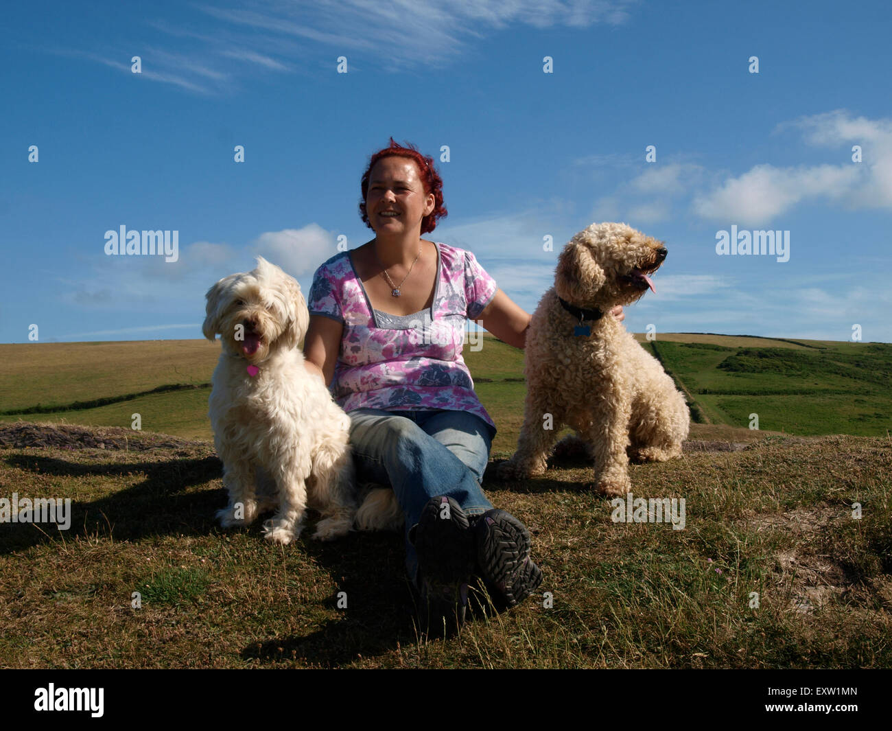 Frau mit Hund saß auf einem Hügel, genießen Sie die Sommersonne, Woolacombe, Devon, UK Stockfoto