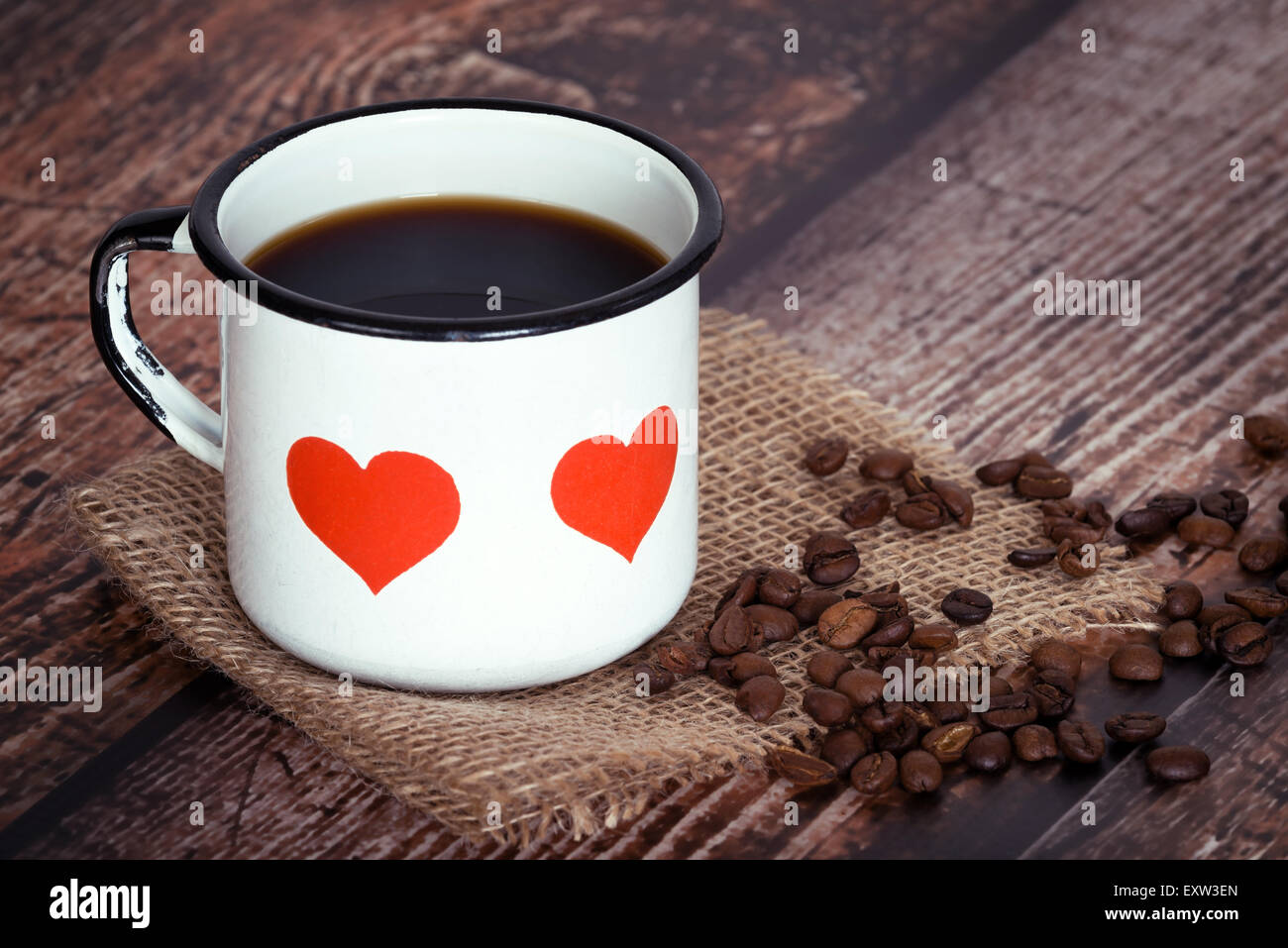 Eine Tasse schwarzen Kaffee in eine alte Emaille Becher mit Herzen, Kaffeebohnen auf Vintage rustikales-Hintergrund Stockfoto
