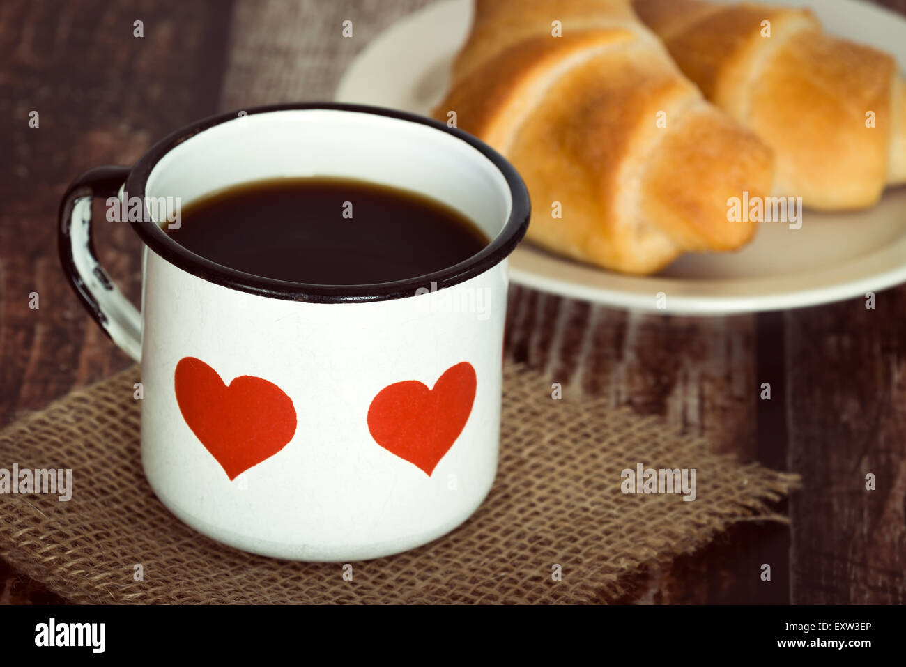Eine Tasse schwarzen Kaffee in eine alte Emaille-Tasse, Frühstückscroissants auf Hintergrund, Vintage rustikalen Tisch Stockfoto