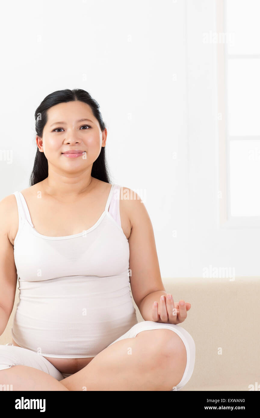 Schwangere Frau sitzt mit den Händen auf die Knie und lächelnd, Stockfoto