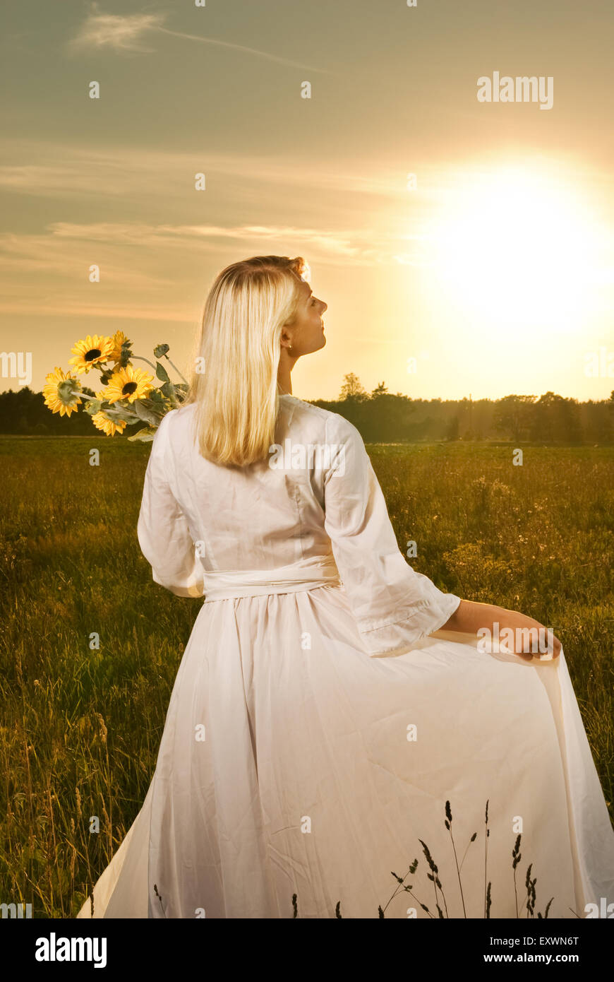 Junge schöne Frau mit einem Strauß von Sonnenblumen im Feld bei Sonnenuntergang Stockfoto