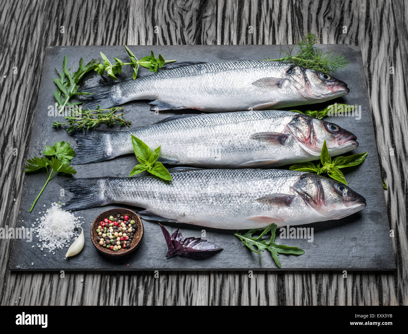 Drei Fische - Wolfsbarsch auf einem Graphit-Brett mit Gewürzen und Kräutern. Stockfoto