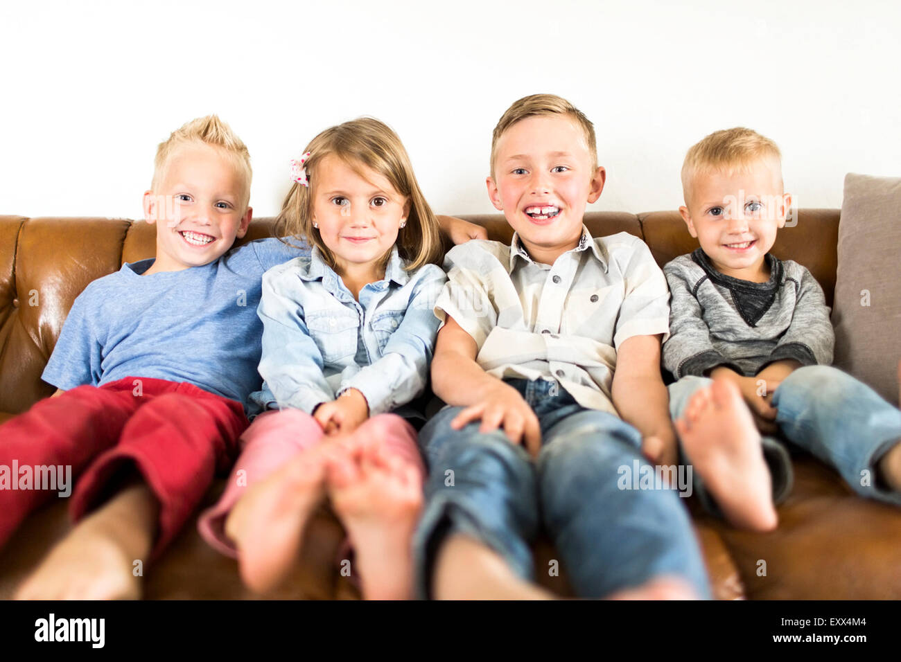 Lächelnde Kinder (2-3, 4-5, 6-7) auf Sofa sitzen Stockfoto