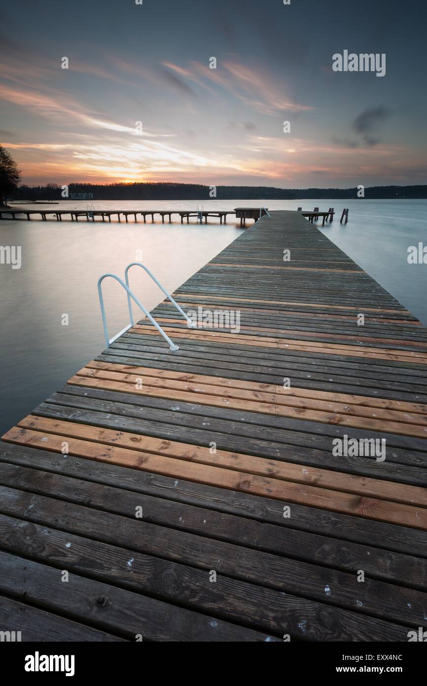 Schöne Seenlandschaft mit Steg. Langzeitbelichtung Fotos mit Filter. Polnische Seeufer bei bewölktem Wetter Sonnenuntergang. Dramatische Stockfoto