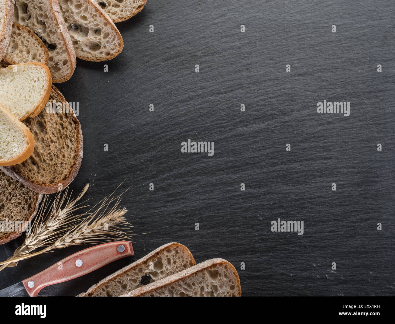 Brotscheiben, ein Weizen und ein Messer auf dem schwarzen Stein Schreibtisch. Stockfoto