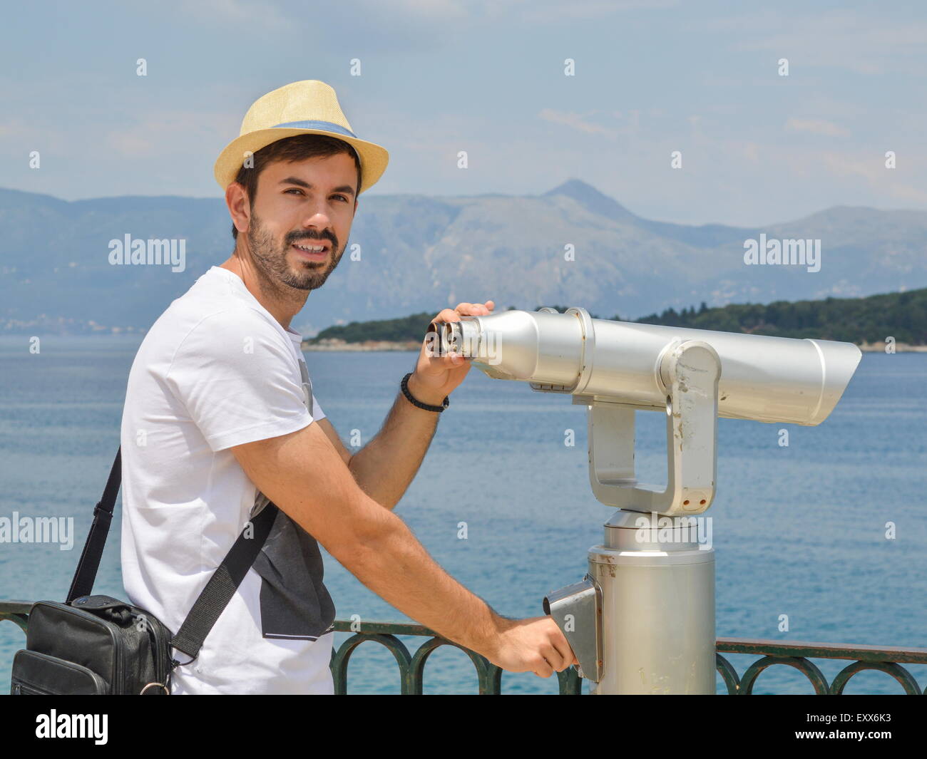 Junge bärtige Mann, hält öffentliche Fernglas am Meer tragen Stroh an einem sonnigen Tag Stockfoto
