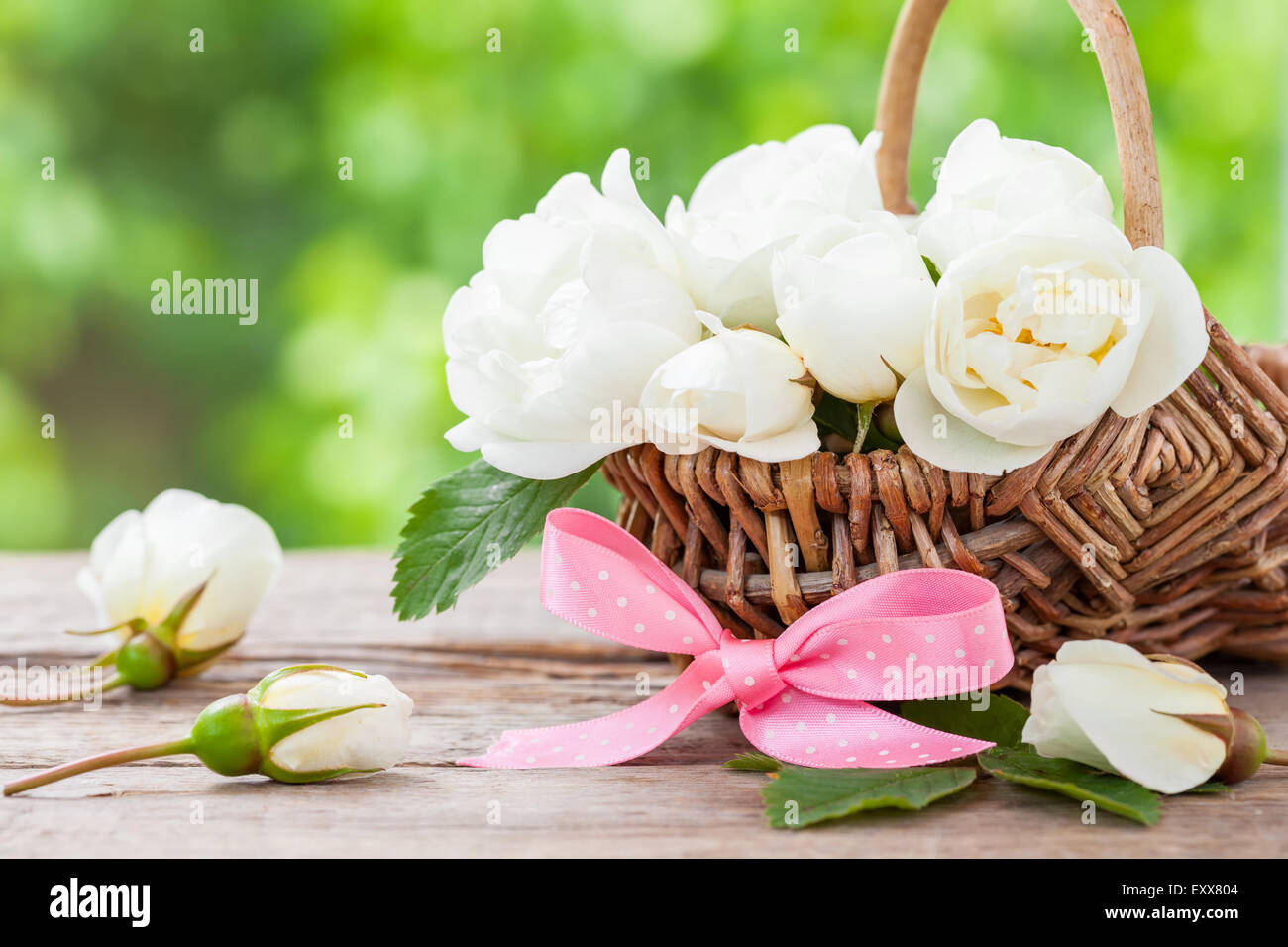 Weidenkorb mit wilden Rosen-Blumen und rosa Schleife. Hochzeit oder Geburtstag Dekoration im rustikalen Stil. Stockfoto