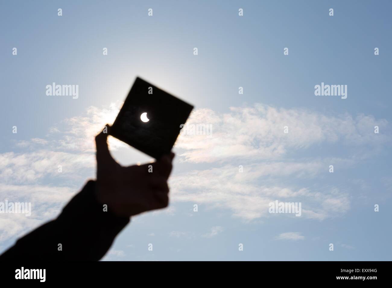 Partielle Sonnenfinsternis. Manndeckung einen starken Sonneneinstrahlung durch dunkle Platte und Sonnenfinsternis zeigt. Mann Hand Silhouette am blauen Himmel. Stockfoto