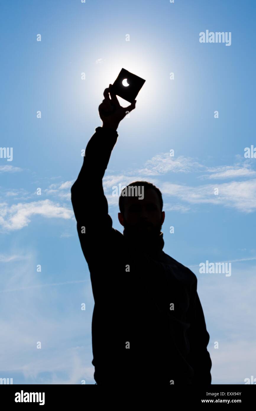 Partielle Sonnenfinsternis. Manndeckung einen starken Sonneneinstrahlung durch dunkle Platte und Sonnenfinsternis zeigt. Mann Hand Silhouette am blauen Himmel. Stockfoto