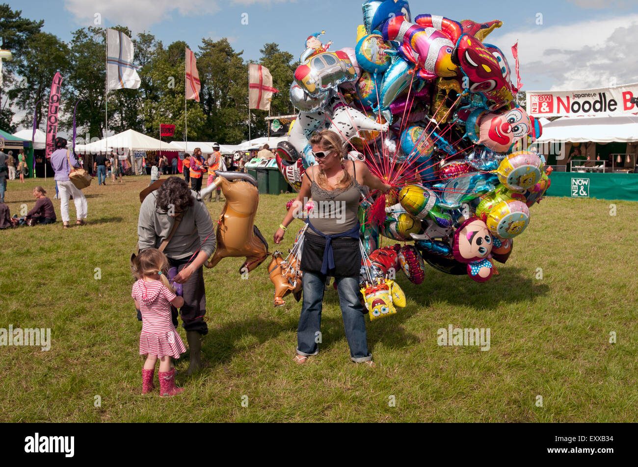 Eine Mutter kauft ihre kleine Tochter einen Ballon von einer Frau mit einem Haufen Luftballons beim Musikfestival WOMAD Welt Stockfoto