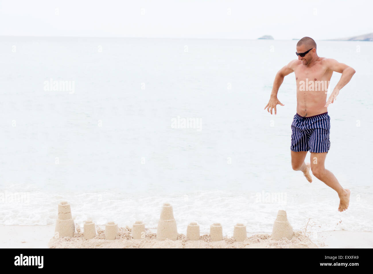 Mann springt am Strand über Sandburg, Meer im Hintergrund Stockfoto