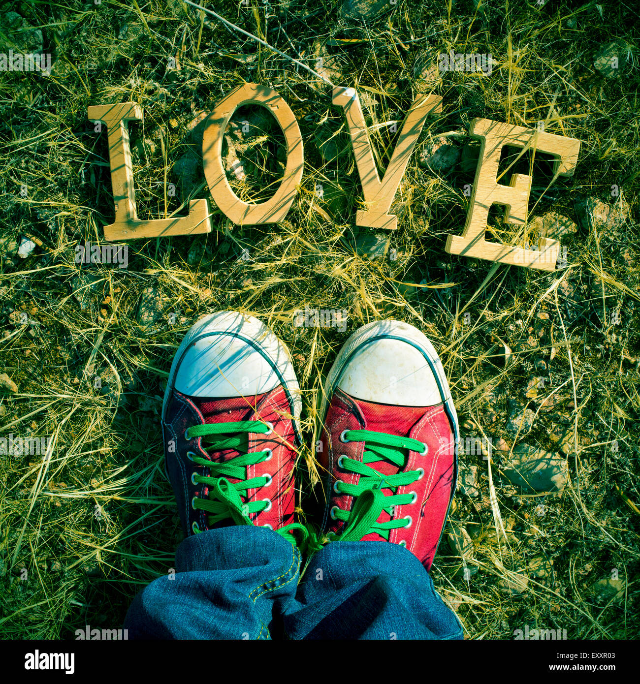Nahaufnahme der Füße eines Mannes tragen rote Turnschuhe treten auf dem Rasen, wo ein Haufen von Holzbuchstaben bilden das Wort Liebe mit Stockfoto