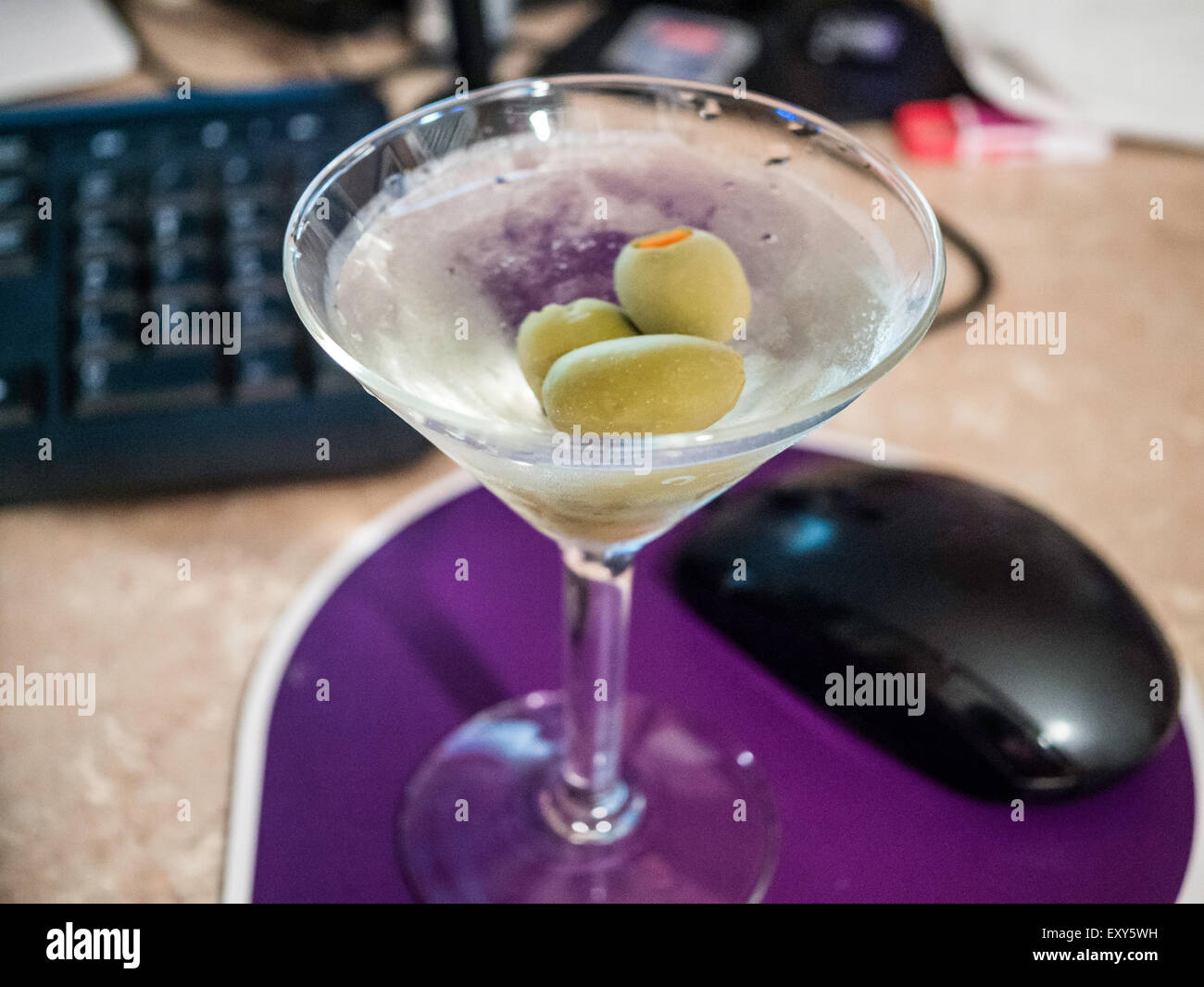 Gin Martini neben Computer-Maus mit Weichzeichner Computertastatur im Hintergrund sitzt. Stockfoto