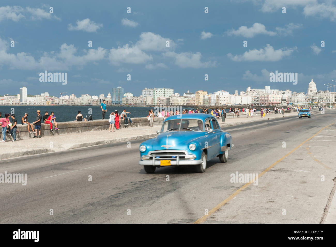 Havanna, Kuba - 18. Mai 2011: Klassisch blau American Taxi fährt neben Massen der Kubaner entspannend auf dem Malecon in Vedado. Stockfoto