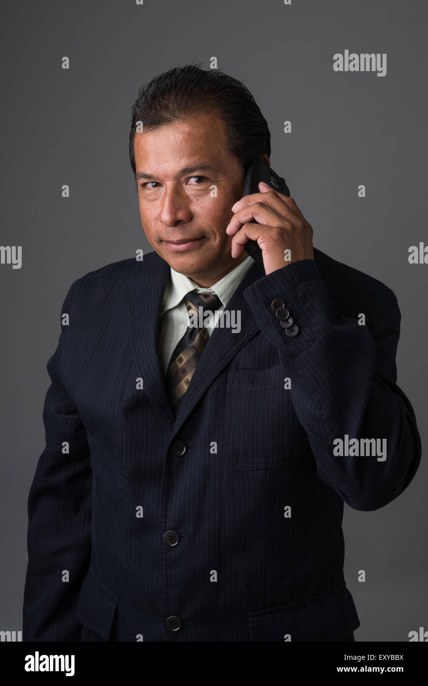 Hispanic Geschäftsmann hält eine Zelle Telefon, Blick in die Kamera und lächelnd leicht. Stockfoto