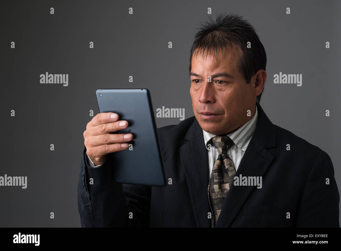 Hispanic Geschäftsmann hält ein Ipad Tablet lesen, auf der Suche, ernst und konzentriert. Stockfoto