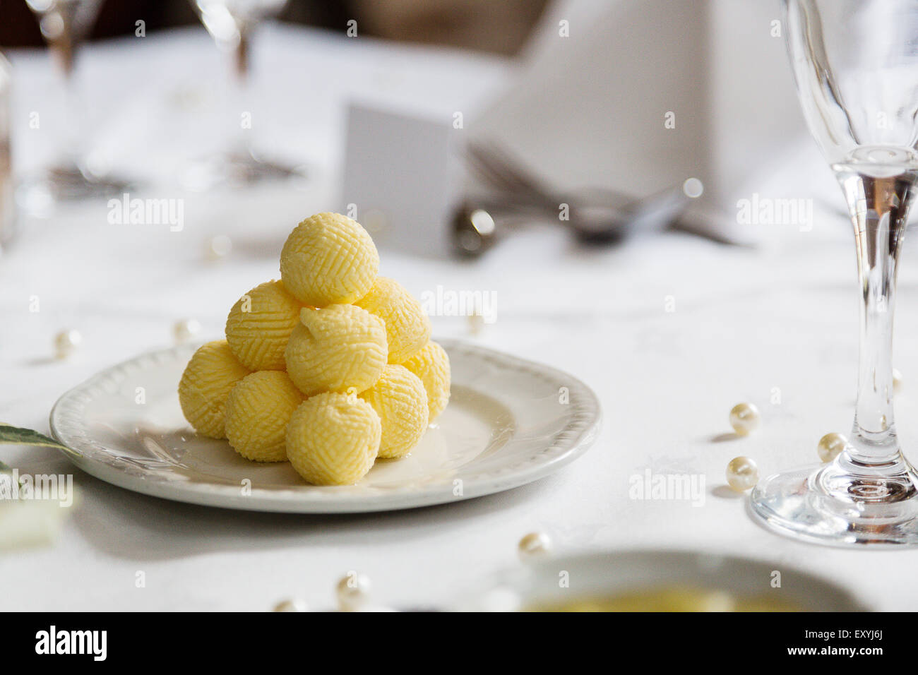 Eine Pyramide von gelben Butter Kugeln auf ein gedeckter Tisch für ein Bankett. Die Kugeln werden auf Teller mit frischen Brötchen verwendet werden serviert. Stockfoto