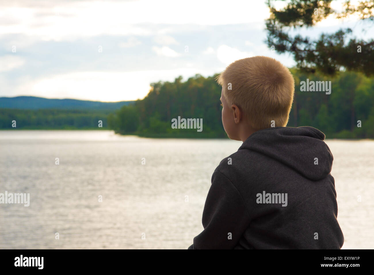 trauriges Kind sitzt allein am See an einem bewölkten Tag Stockfoto